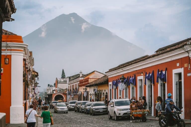 Street scene in Antigua Guatemala of colorful red buildings and cobblestone with a silhouetted volcano in the background