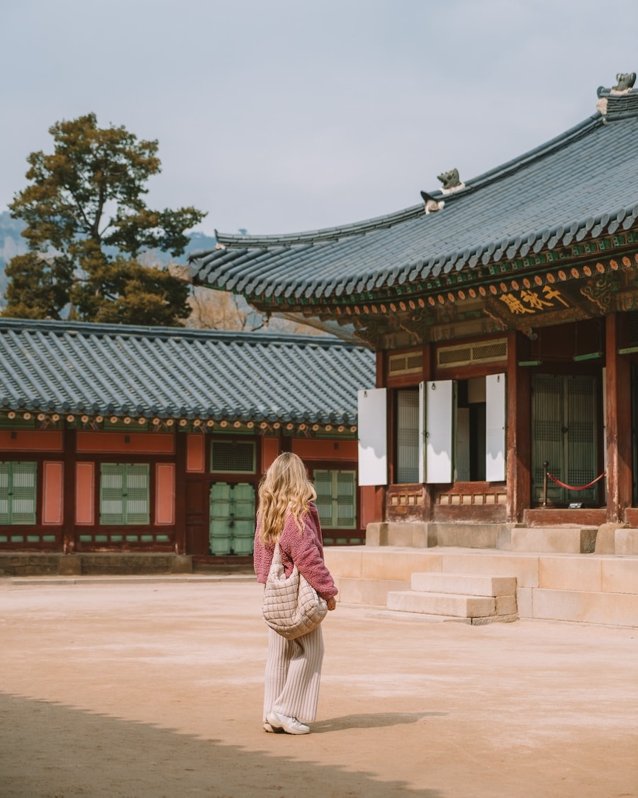 Michelle Halpern in all pink outfit standing in a lone courtyard inside a palace in Seoul looking at the buildings