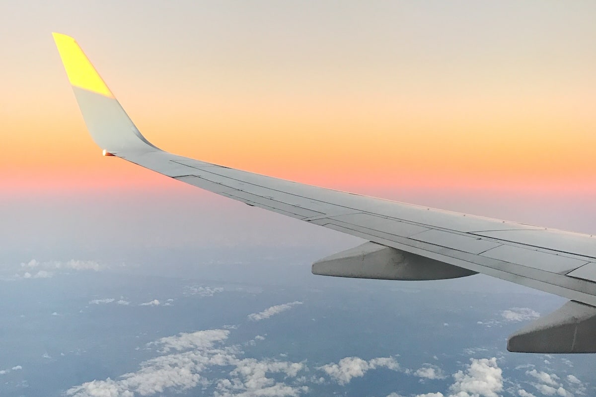 airplane wing view sunset Airplane wing with clouds below and orange yellowish sunset behind it