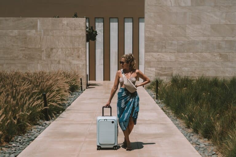 Michelle Halpern in a bikini and sarong standing next to a blue suitcase