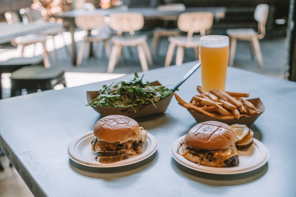burgers fries salad Table set up with two burgers, salad, fries and a beer from Third Window Brewing