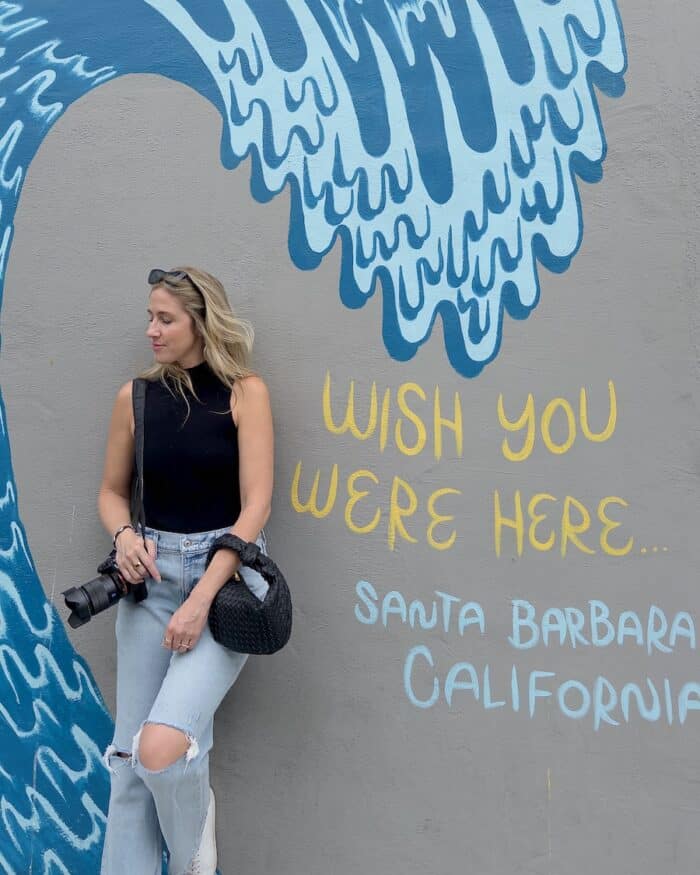 Wish you were here Santa Barbara Michelle Halpern standing up against a wall that says "Wish you were here. Santa Barbara, California"