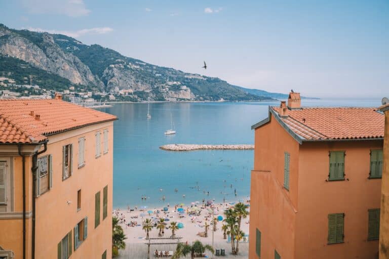 View looking out from orange-hued buildings in Menton, France out onto the beach