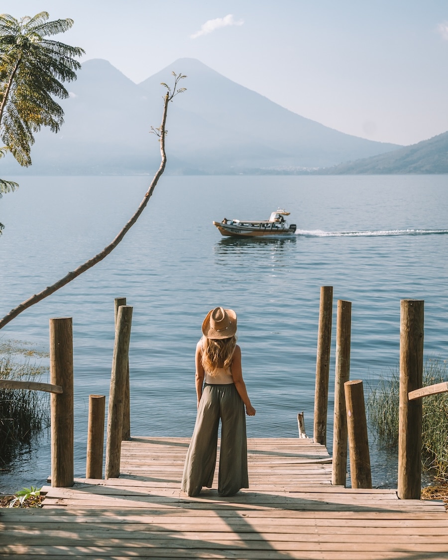 dock in San Marcos La Lagun Michelle Halpern standing on a serene dock in San Marcos La Laguna with volcanoes in the distance and a boat cruising through the lake