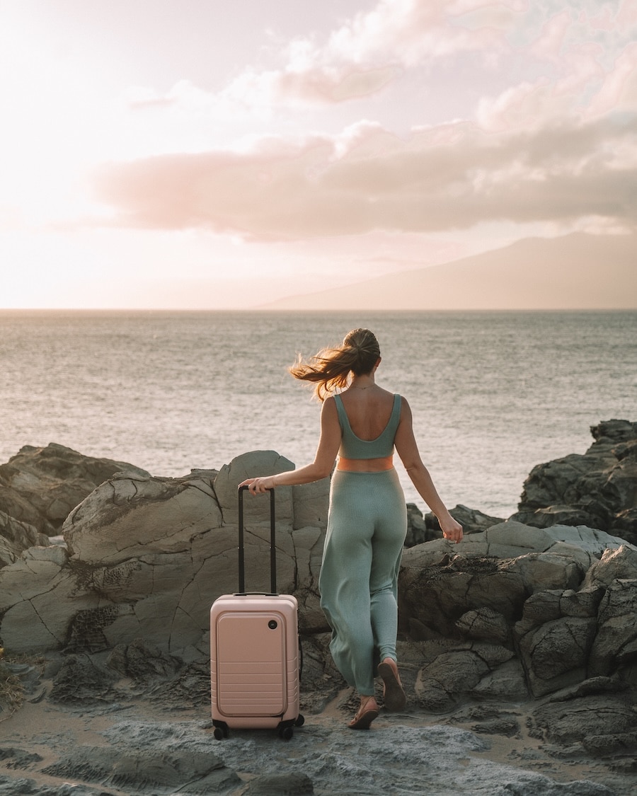 pink suitcase hawaii Michelle Halpern holding the handle of a pink suitcase along a rocky area in Hawaii | What To Pack For A Beach Vacation